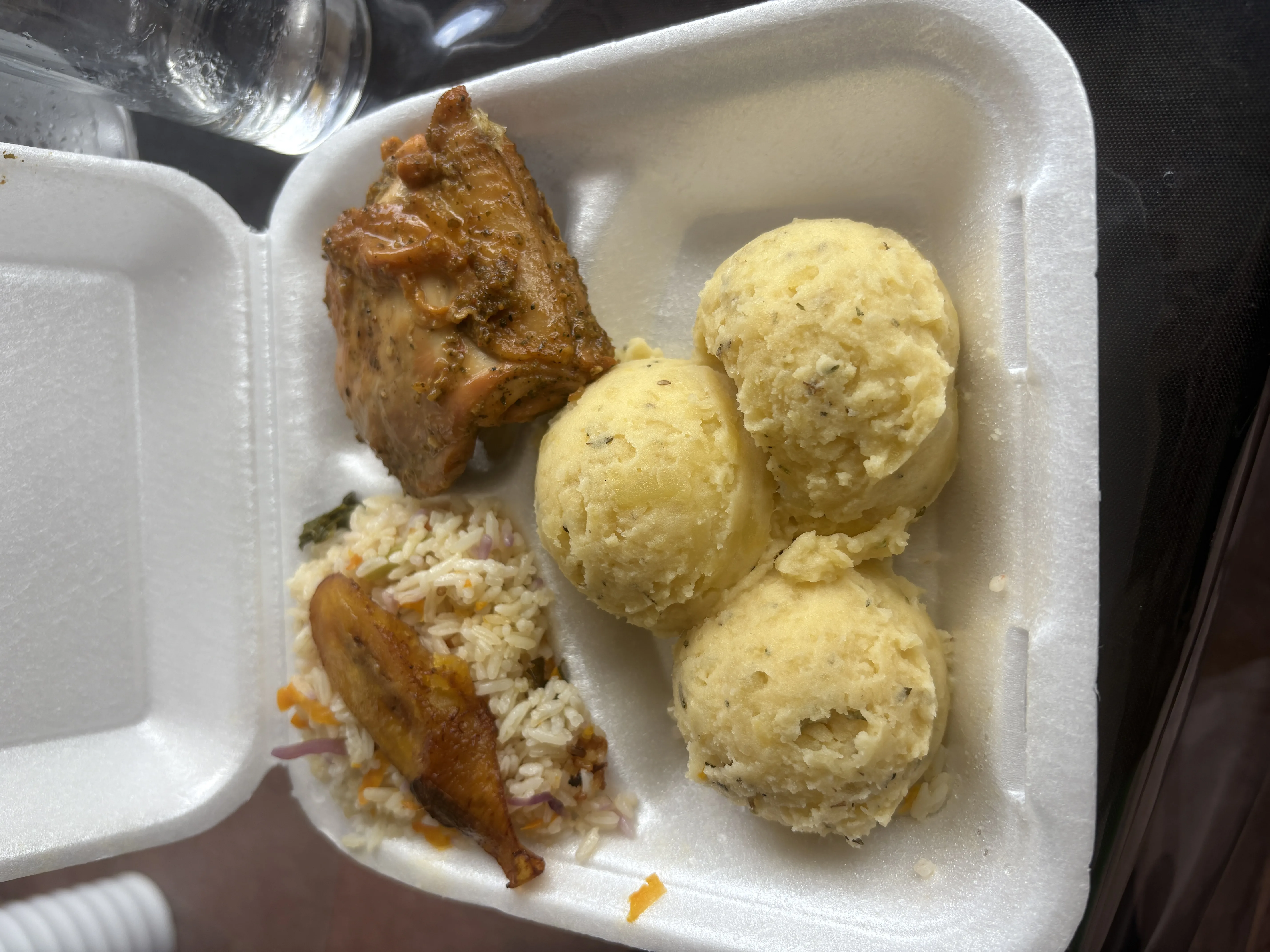 Caja para llevar con pollo, arroz, plátano y porciones de puré de papa.