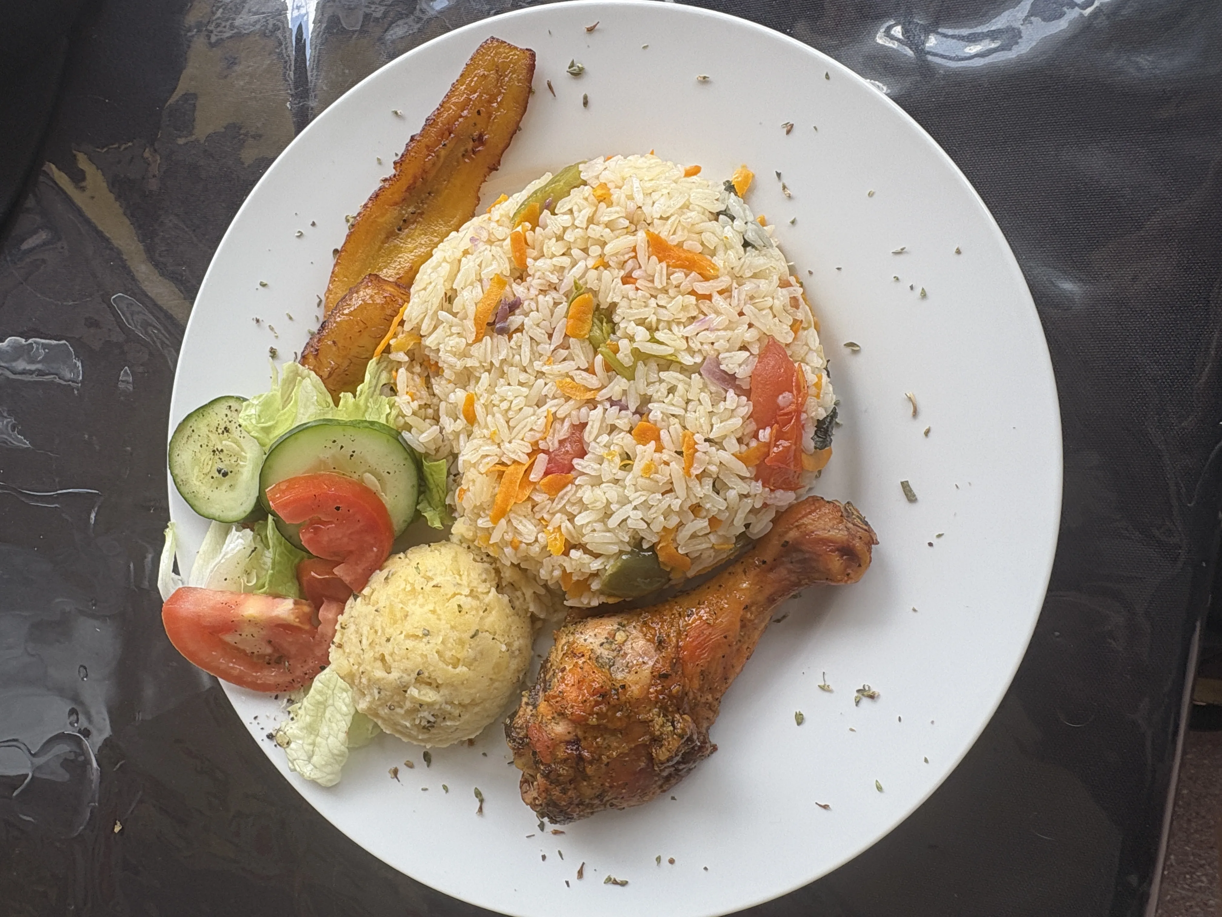 Pollo asado con arroz, plátano, ensalada y puré en plato blanco.