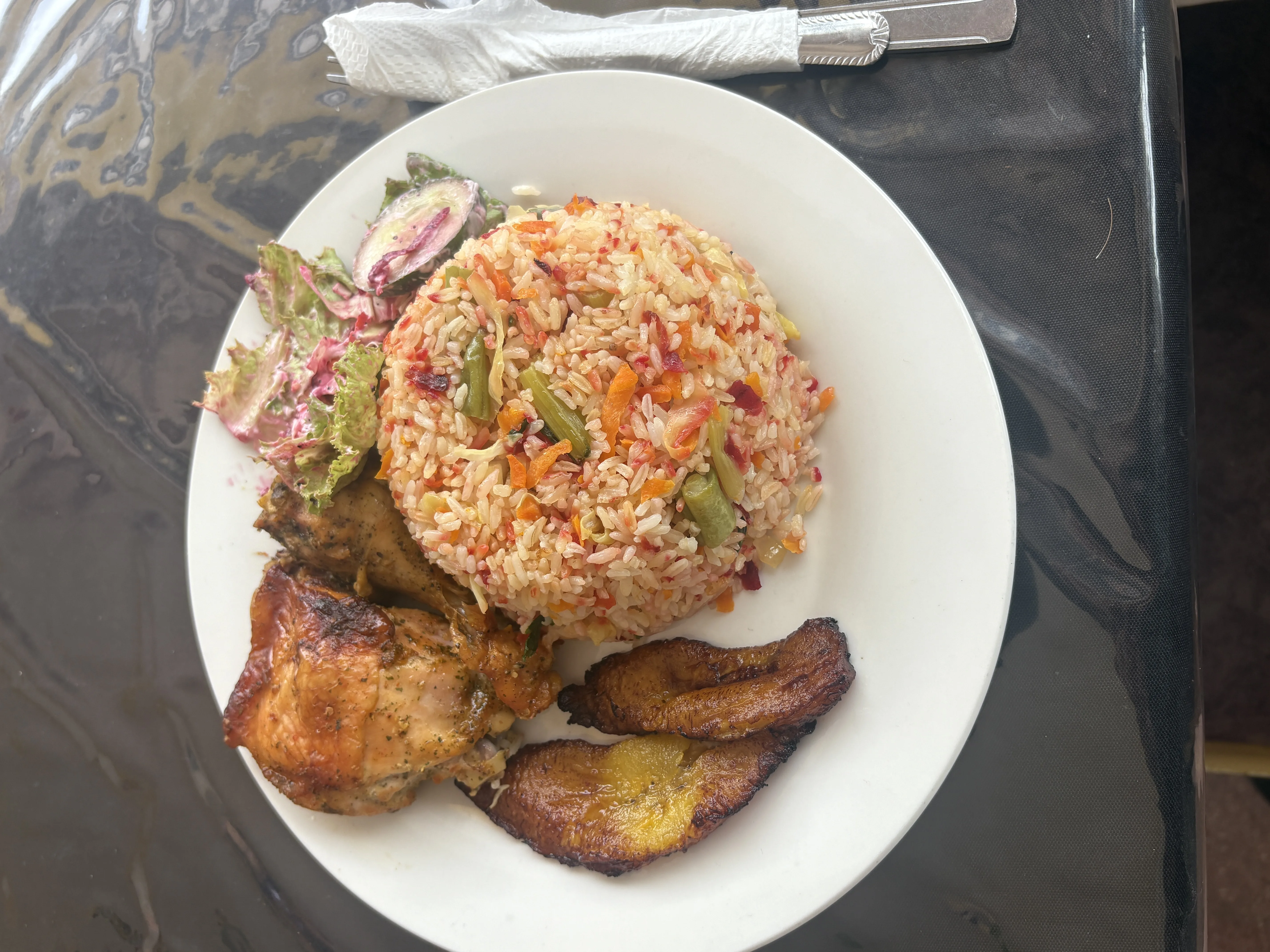 Pollo asado, arroz con vegetales, plátano maduro y ensalada en plato blanco.